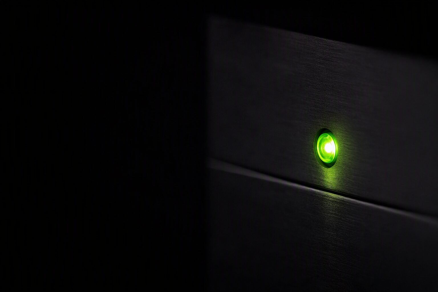 A single green status light glowing on a dark brushed-metal panel